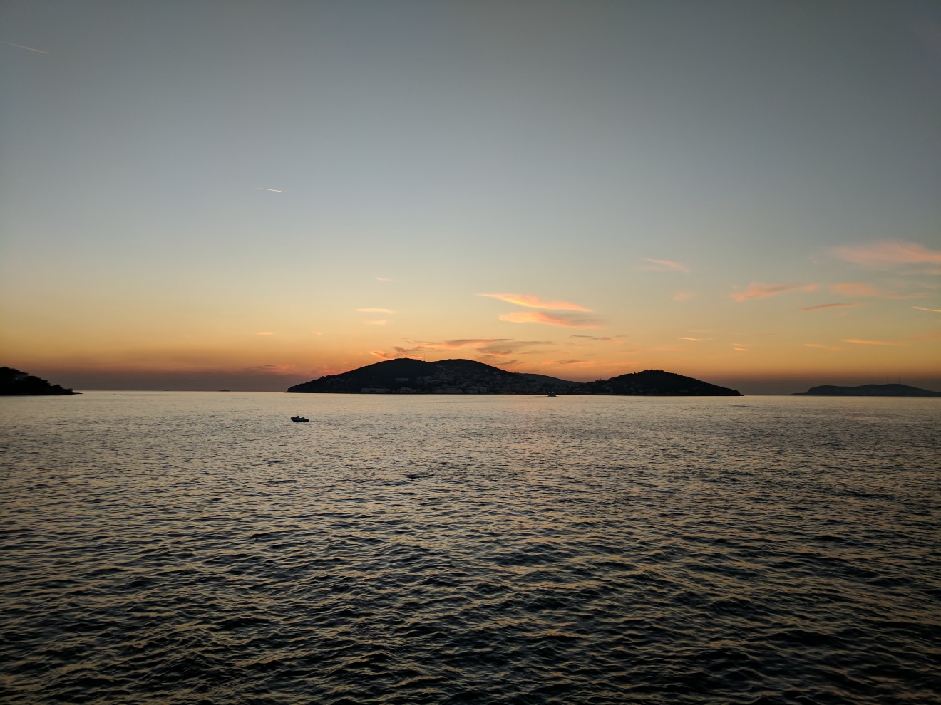 Islands at sunset. The islands are silhouetted against a pastel sky, with a few clouds illuminated with the dying embers of the sun. The foreground is the sea, with lots of uniform but small waves.
