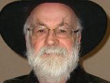 A photo of a white man. He has a short white beard and is wearing glasses and a wide-brimmed hat.