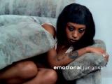 A Black woman, curled up on a sofa; the grey sofa cushion is covering most of her body like a comfort blanket. She looks to be in a great deal of emotional turmoil.