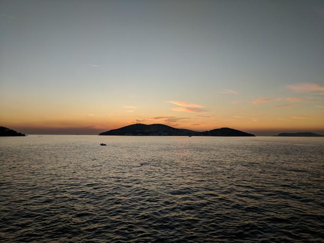 Islands at sunset. The islands are silhouetted against a pastel sky, with a few clouds illuminated with the dying embers of the sun. The foreground is the sea, with lots of uniform but small waves.