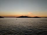 Islands at sunset. The islands are silhouetted against a pastel sky, with a few clouds illuminated with the dying embers of the sun. The foreground is the sea, with lots of uniform but small waves.